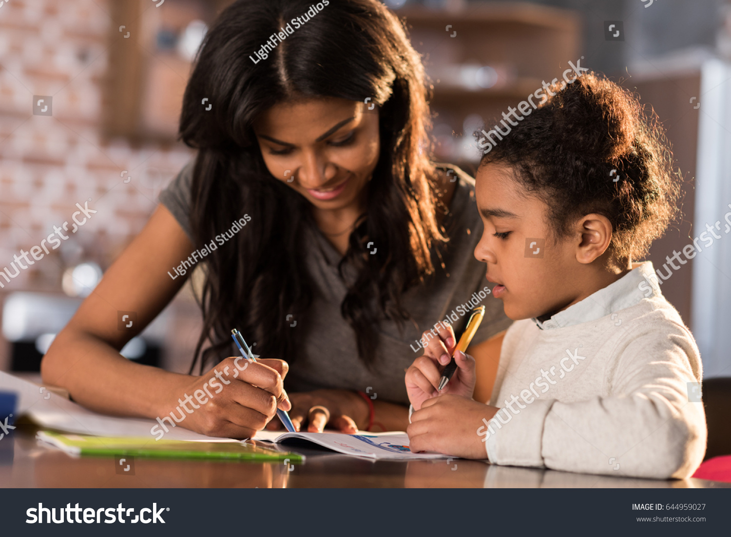 Mother and cute little daughter sitting at table and doing homework together at home, homework help concept #644959027