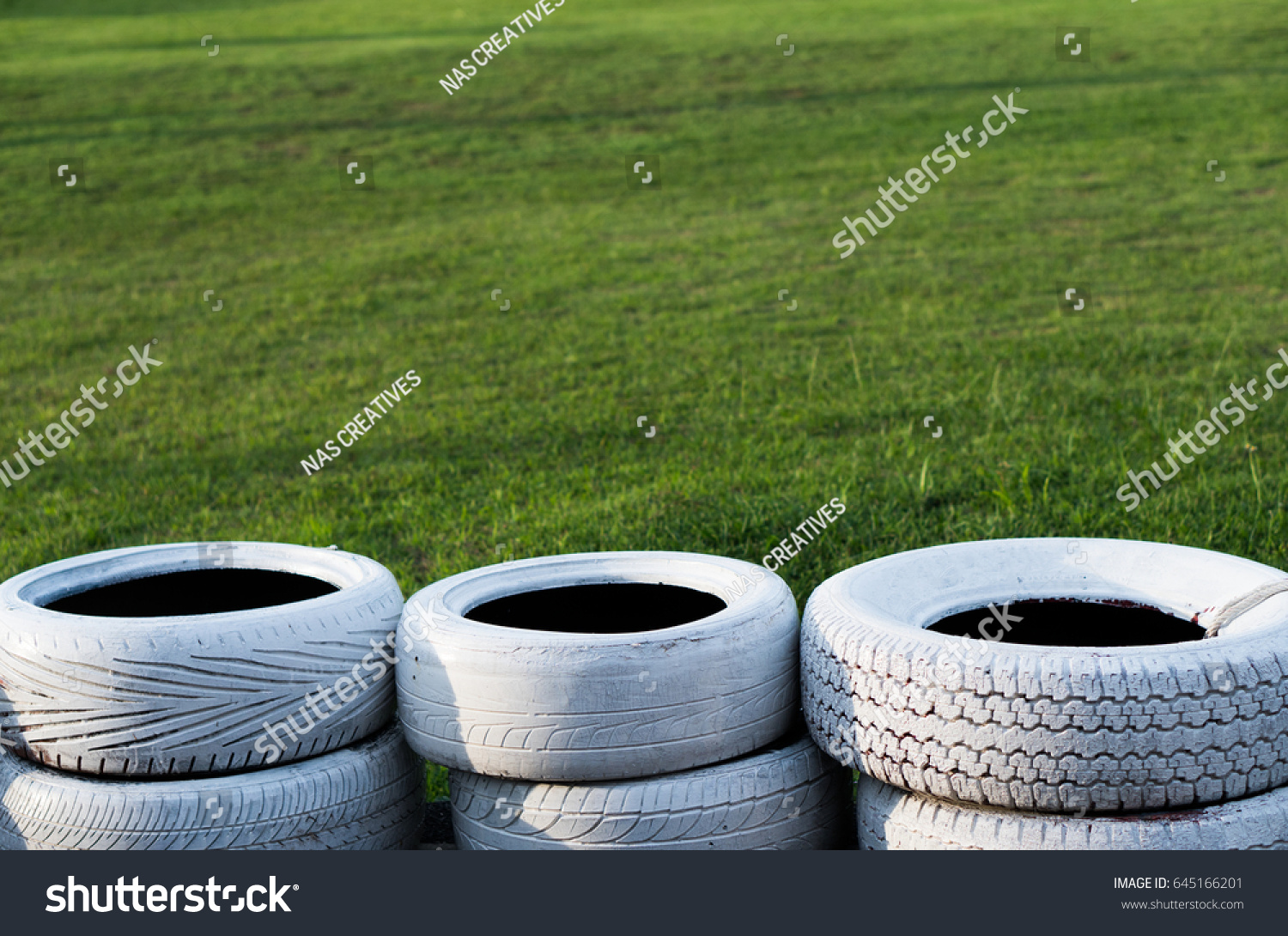 Painted white old tires on kart race course over green grass background #645166201