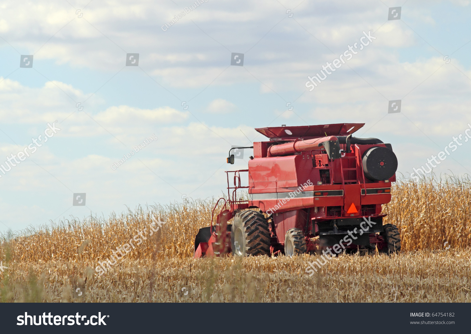 Red combine harvesting a farm field of corn #64754182