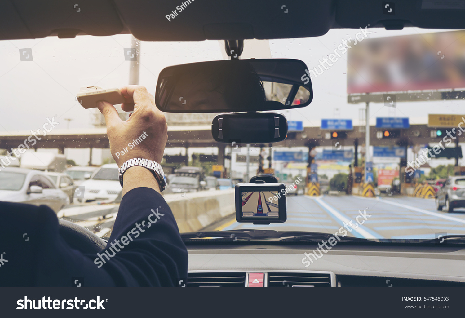 Man driving car using navigator and holding electronic toll collection system device #647548003