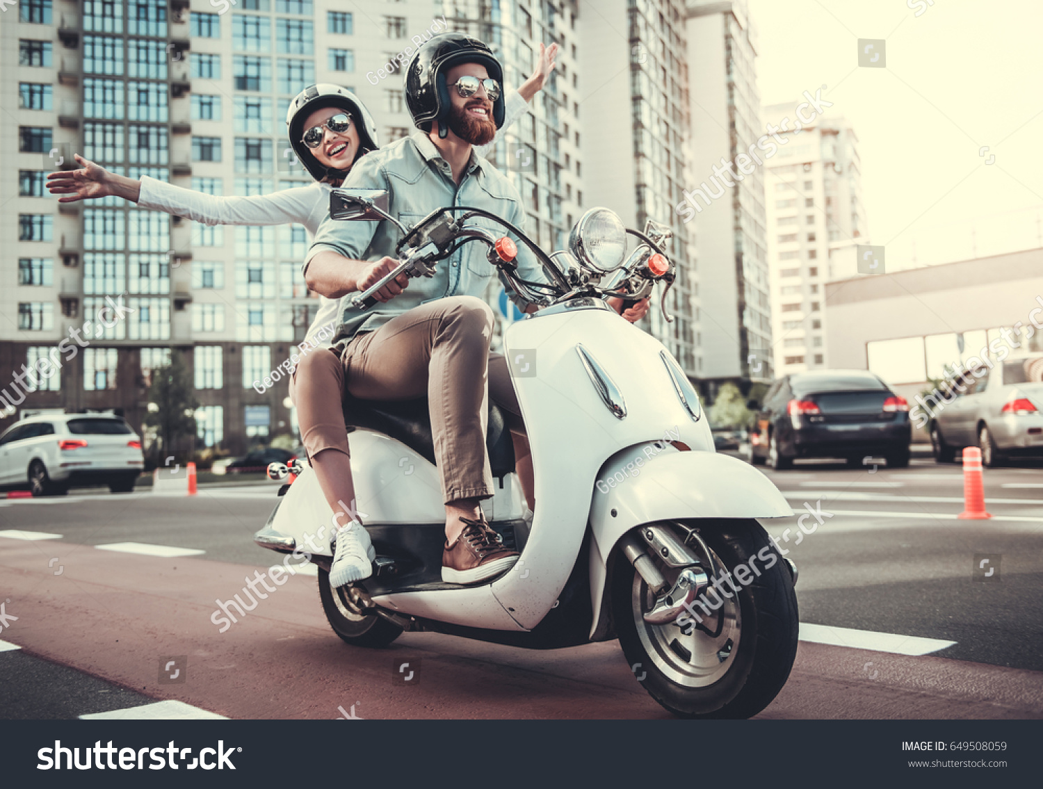 Beautiful young couple in sun glasses and helmets is smiling while riding a scooter #649508059