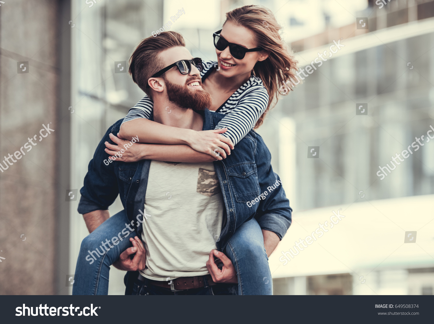 Beautiful young couple in sun glasses looking at each other and smiling while standing outdoors. Girl piggyback #649508374