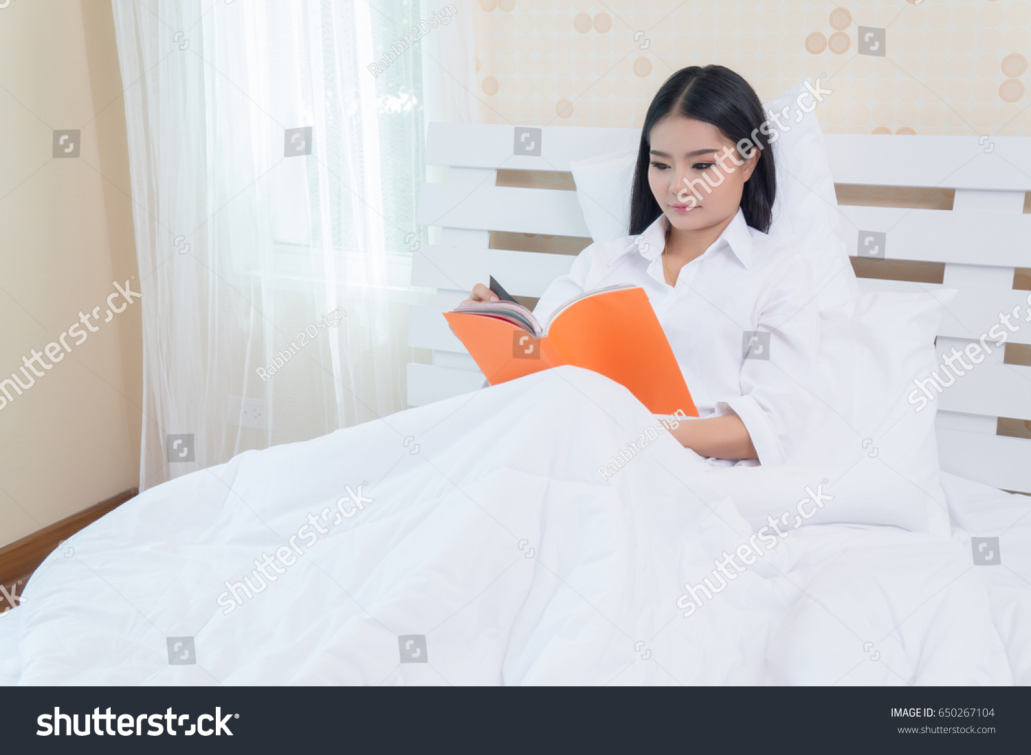Woman lying in bed while reading a book #650267104