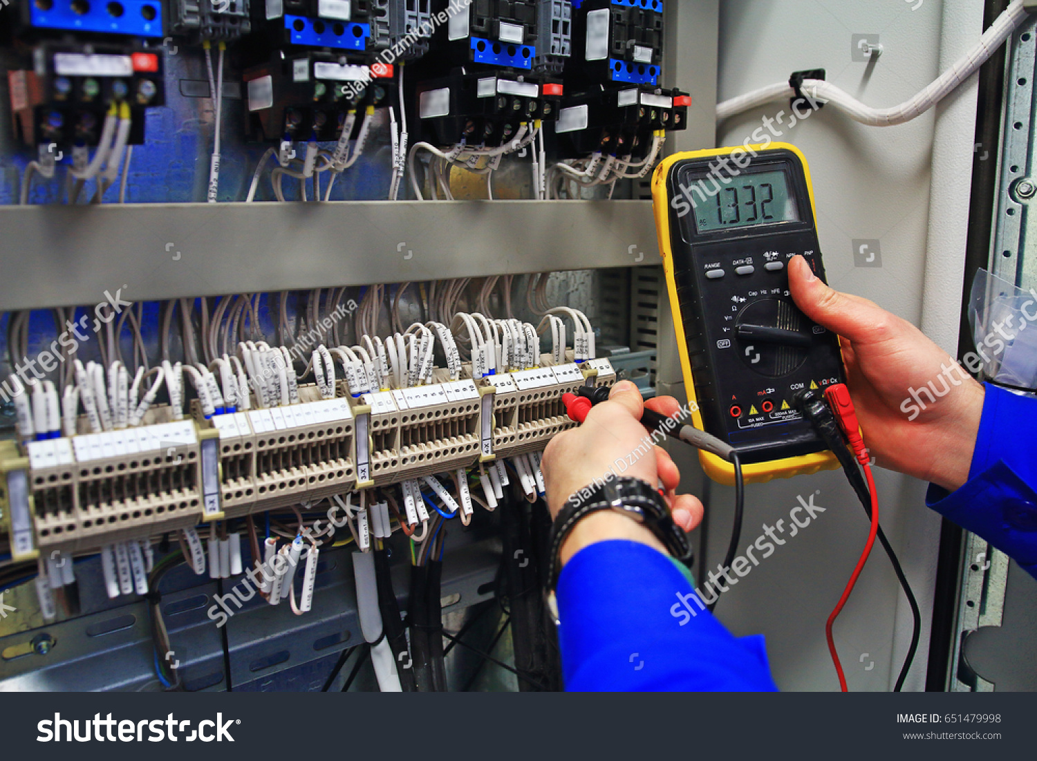 engineer tests the industrial electrical circuits with a multimeter in the control terminal box. Engineer's hands with a multimeter close-up against background of terminal rows of automation panel. #651479998