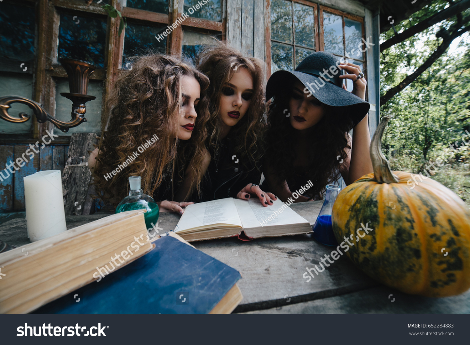 Three vintage witches perform magic ritual, at the table, reading a magical book on the eve of Halloween #652284883