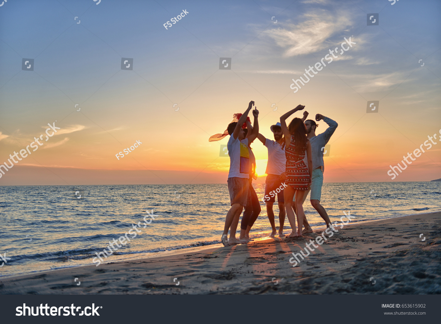 group of happy young people dancing at the beach on beautiful summer sunset #653615902