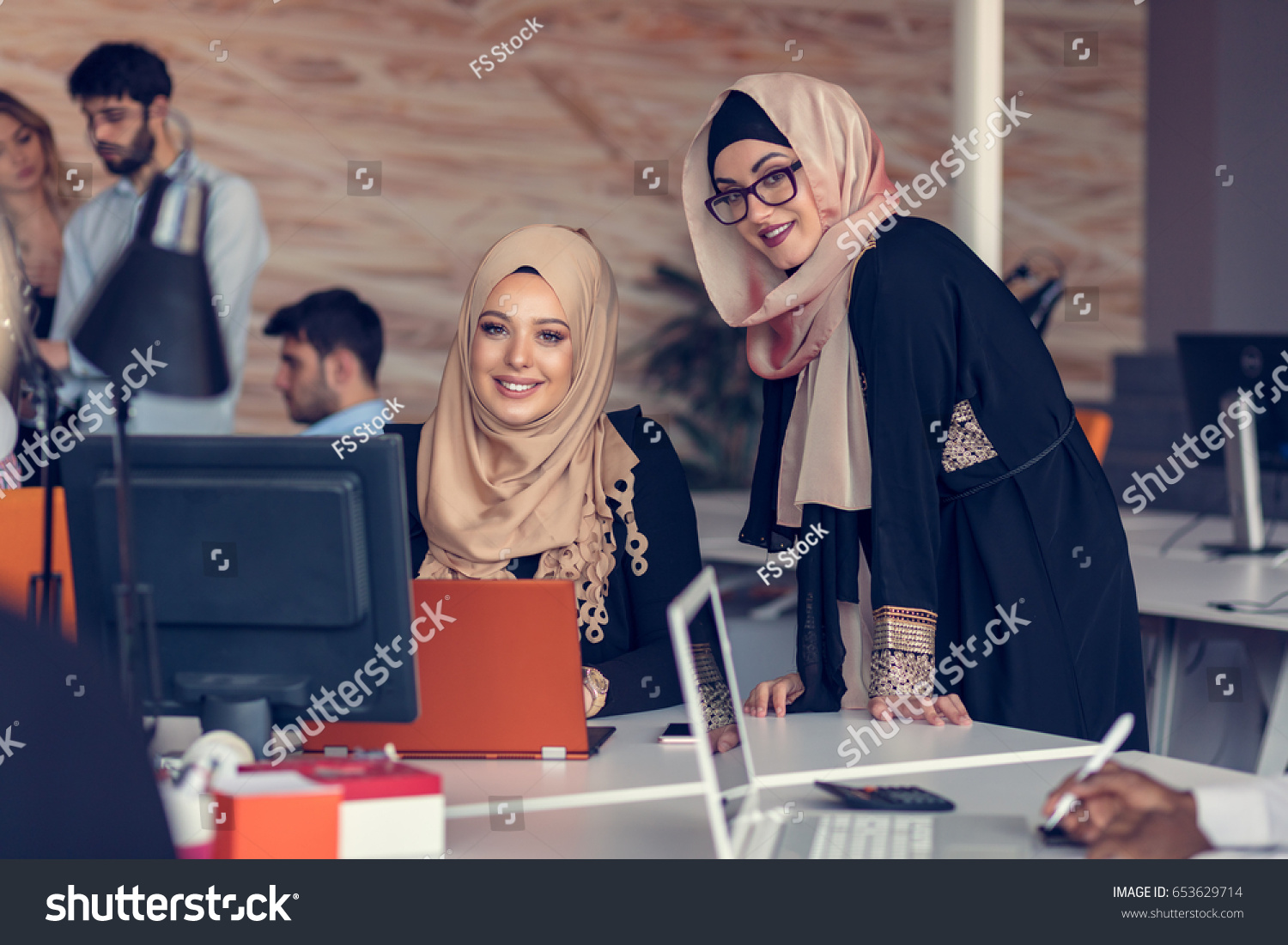 Two woman with hijab working on laptop in office. #653629714