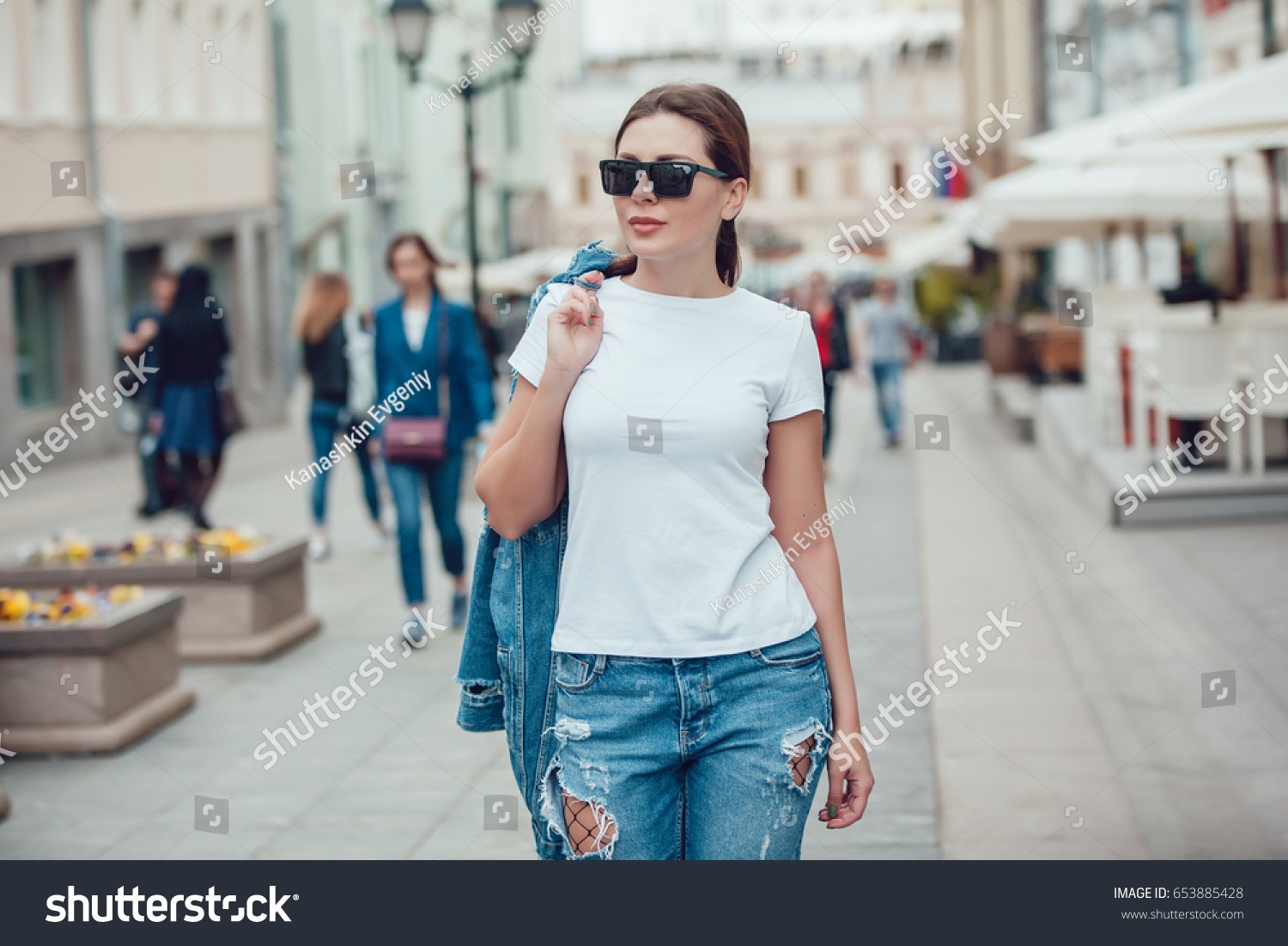 Attractive girl in sunglasses walking along the street. White t-shirt. Mock-up. #653885428
