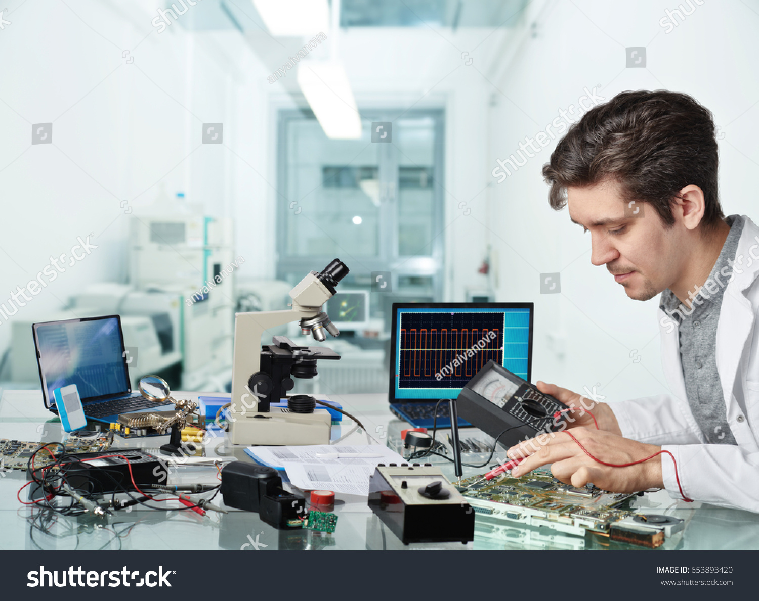 Young energetic male tech or engineer repairs electronic equipment in research facility. Shallow DOF, focus on the face of the worker. #653893420