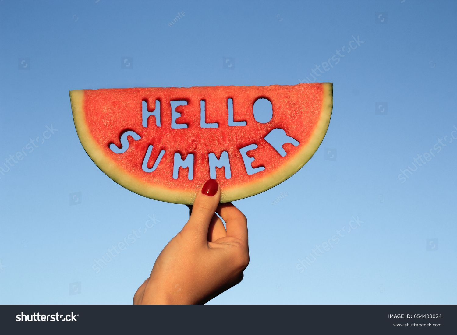 Watermelon slice  with text Hello Summer,  woman hands holding it against blue sky. Summertime concept. #654403024