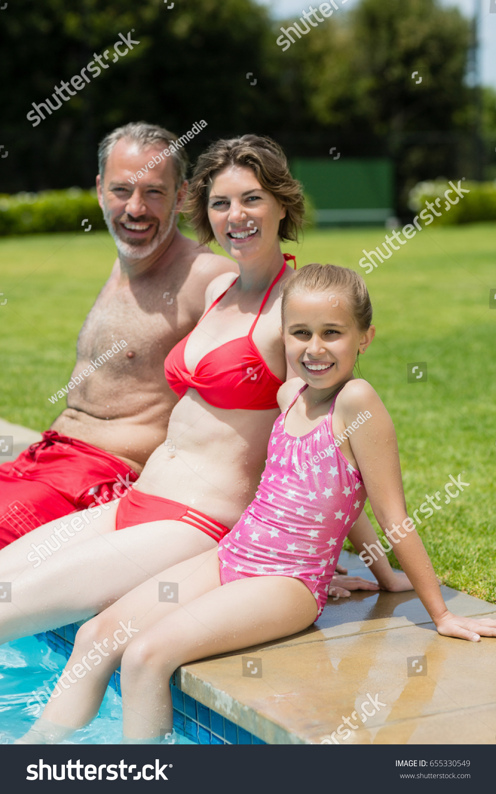 Portrait of parents and daughter sitting on poolside in pool water on a sunny day #655330549