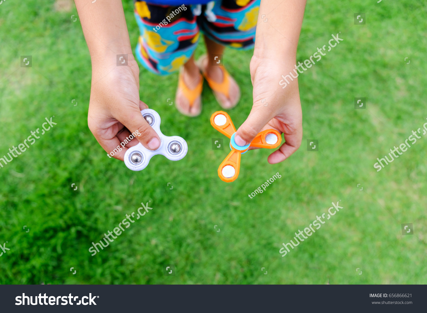 Boy holding play two fidget spinners, Fidget spinner white and orange color spinning stress relieving toy on green grass background.  #656866621