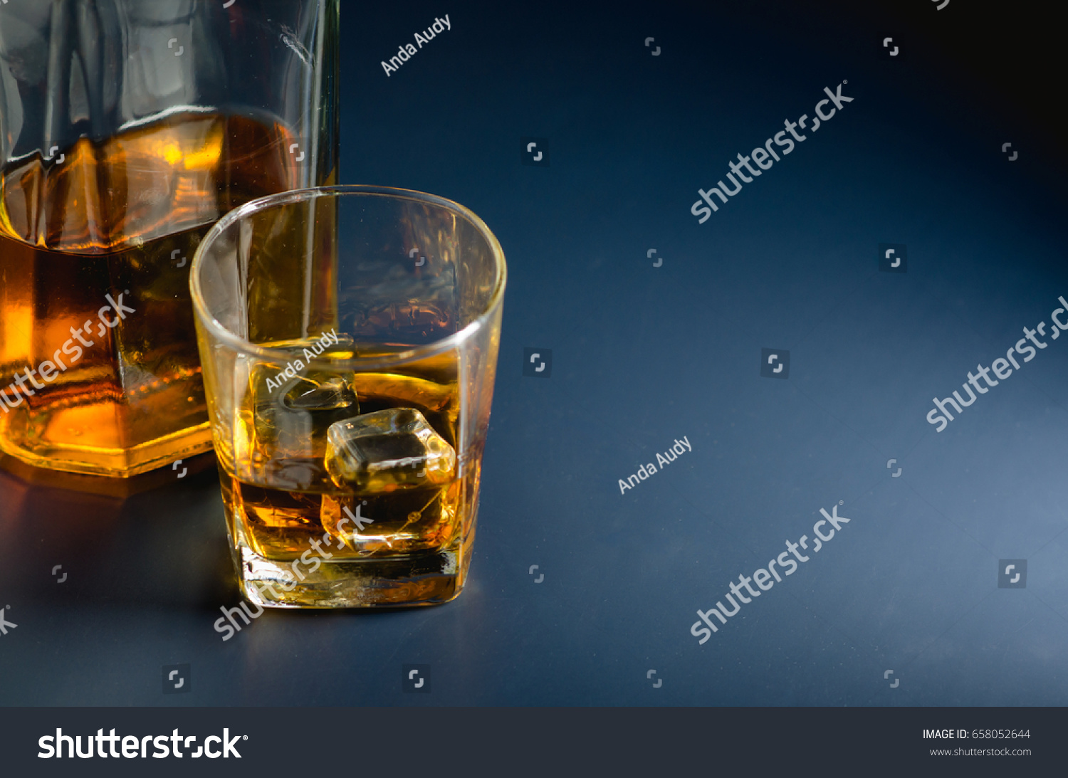 Whiskey glass and bottle on black and blue surface. #658052644