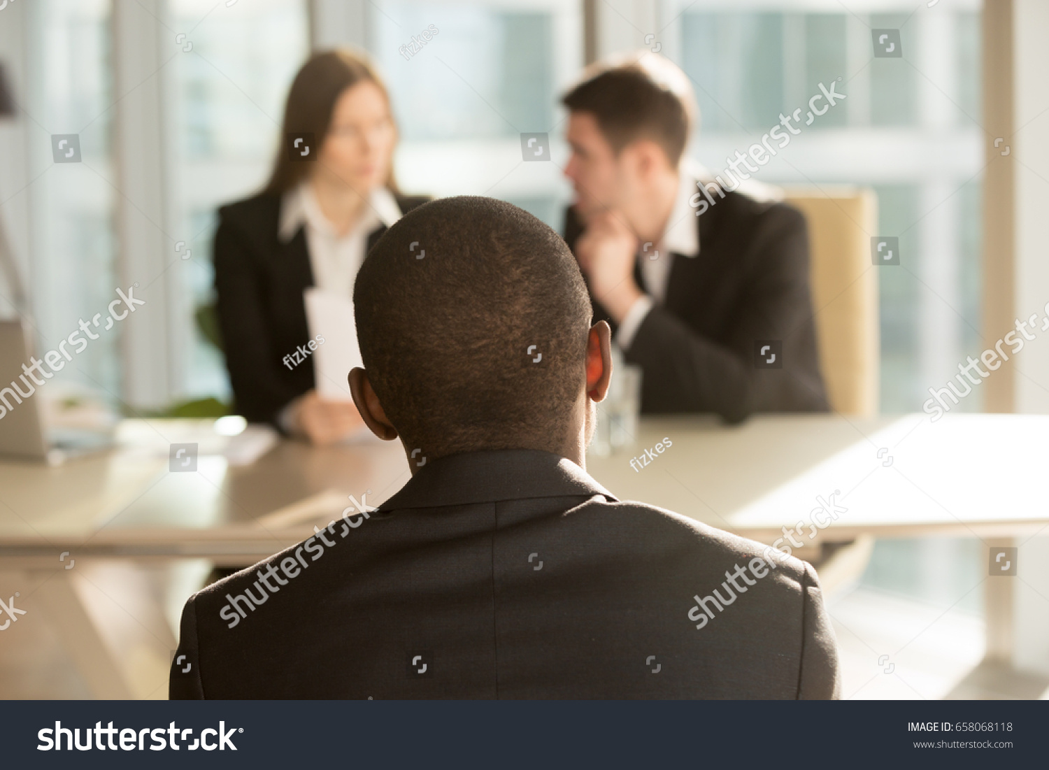 Nervous african-american applicant waiting for result after job interview, hr managers making decision at background, black businessman patiently awaits for claim complaint consideration, back view #658068118