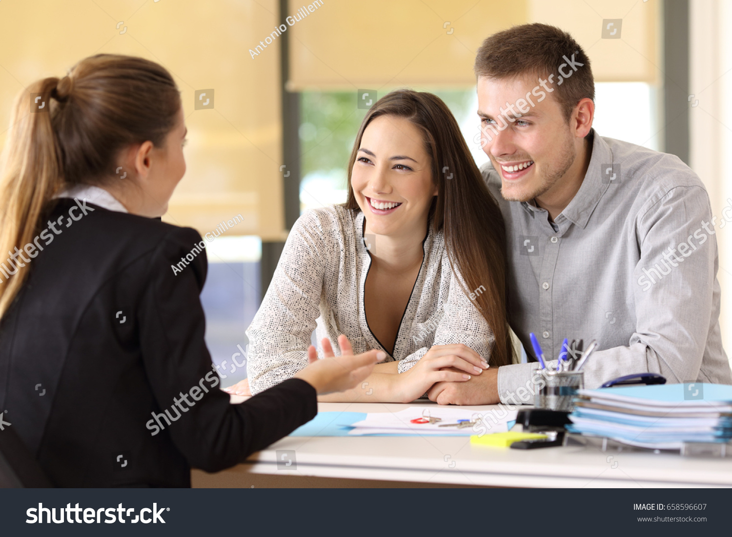 Happy couple talking with a real estate agent at office #658596607