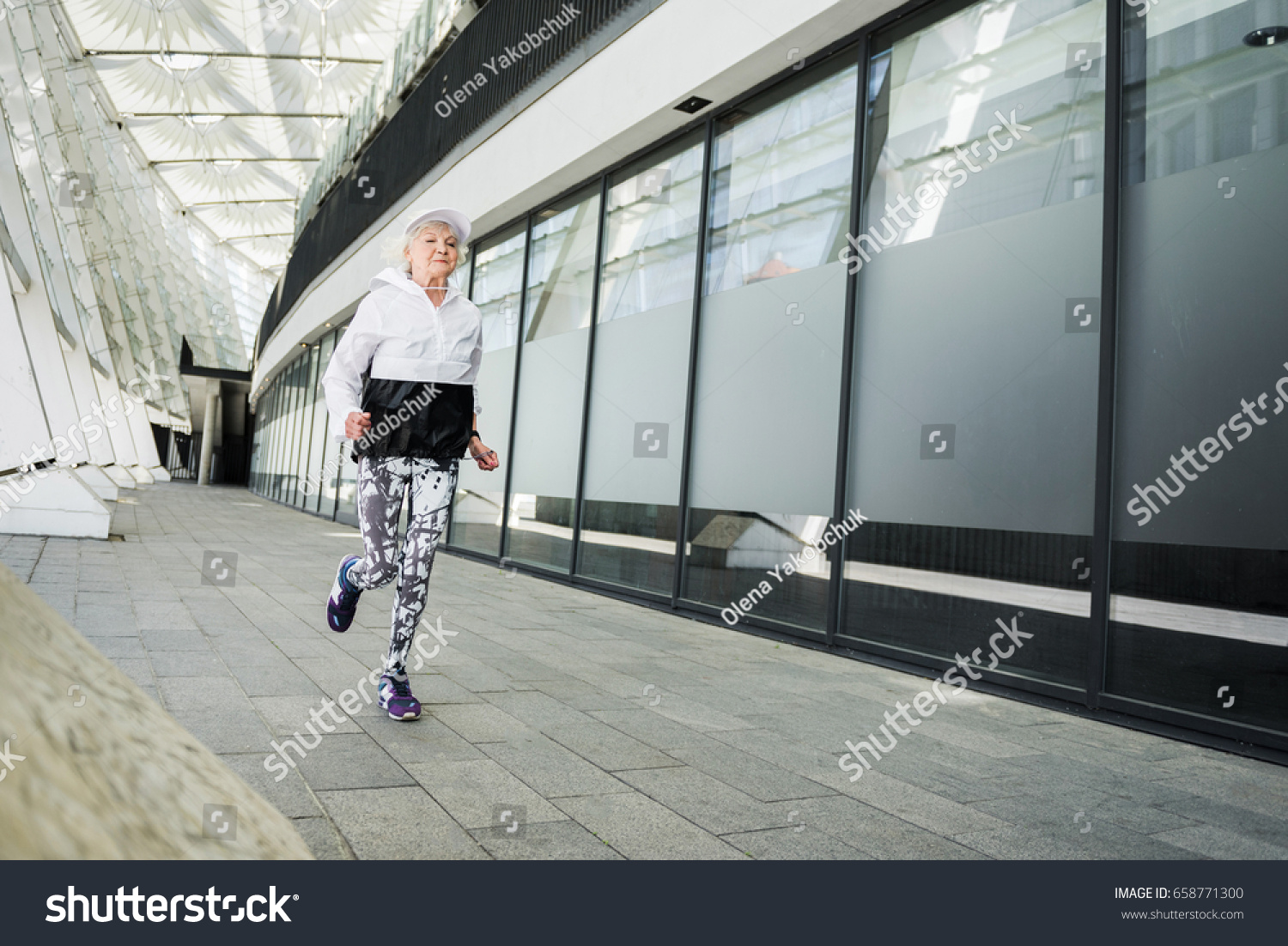 Serious fit old lady running along modern city building #658771300