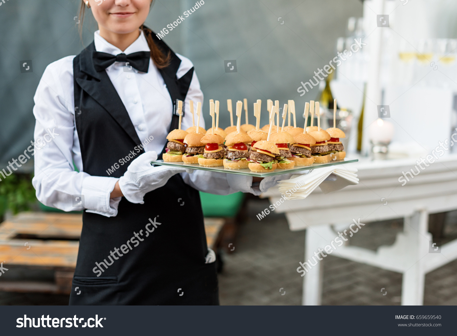 Catering service. Waiter carrying a tray of appetizers. Outdoor party with finger food, mini burgers, sliders. #659659540
