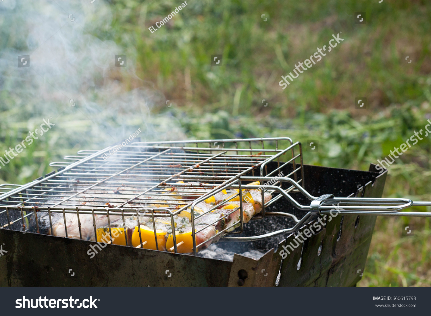fish with vegetables and sweet pepper prepared on the grill grate in the iron grill in the garden during the summer sunny day #660615793