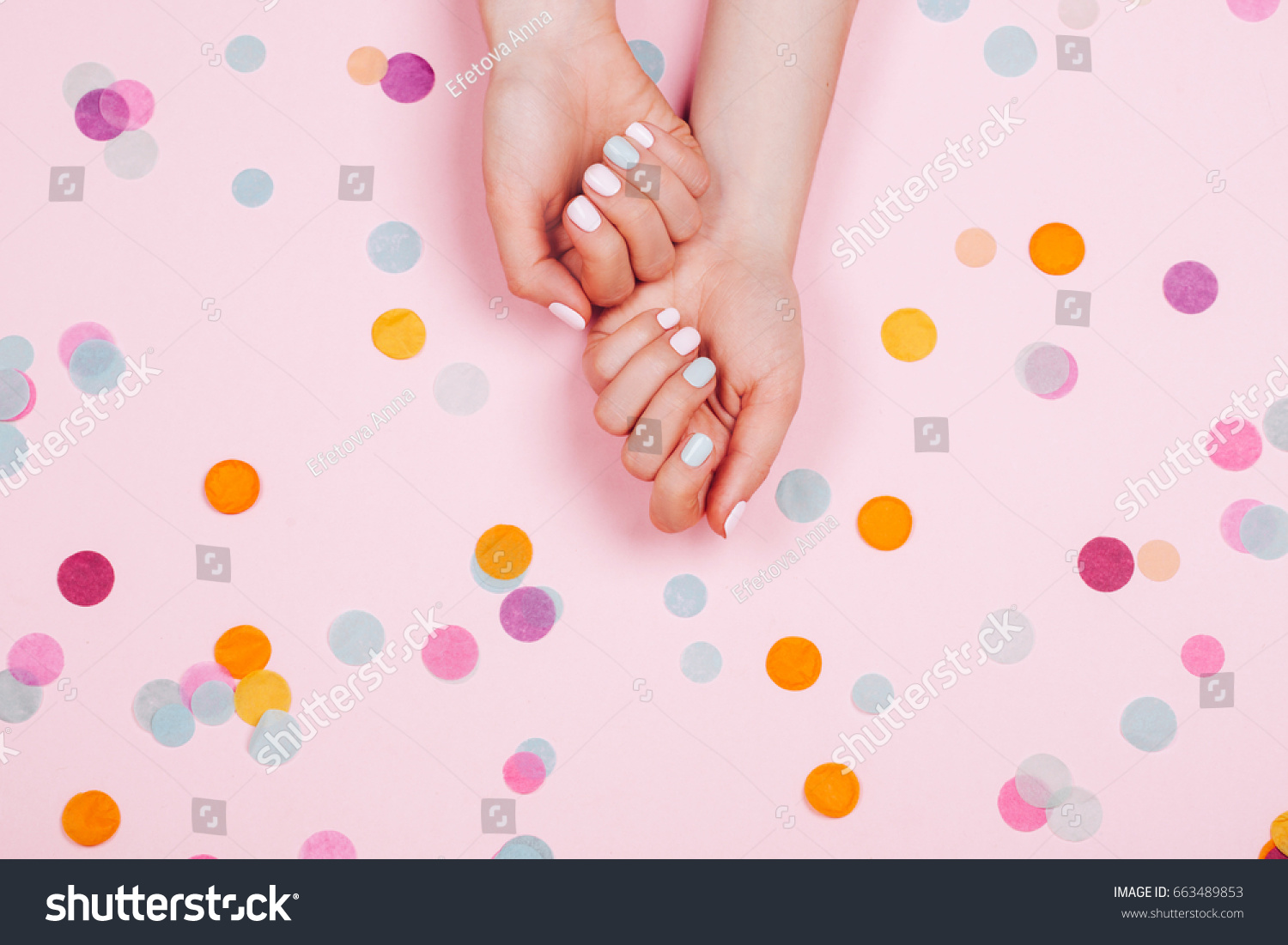 Stylish trendy female pink and blue manicure. Beautiful young woman's hands on pink pastel background with festive multicolored confetti. #663489853