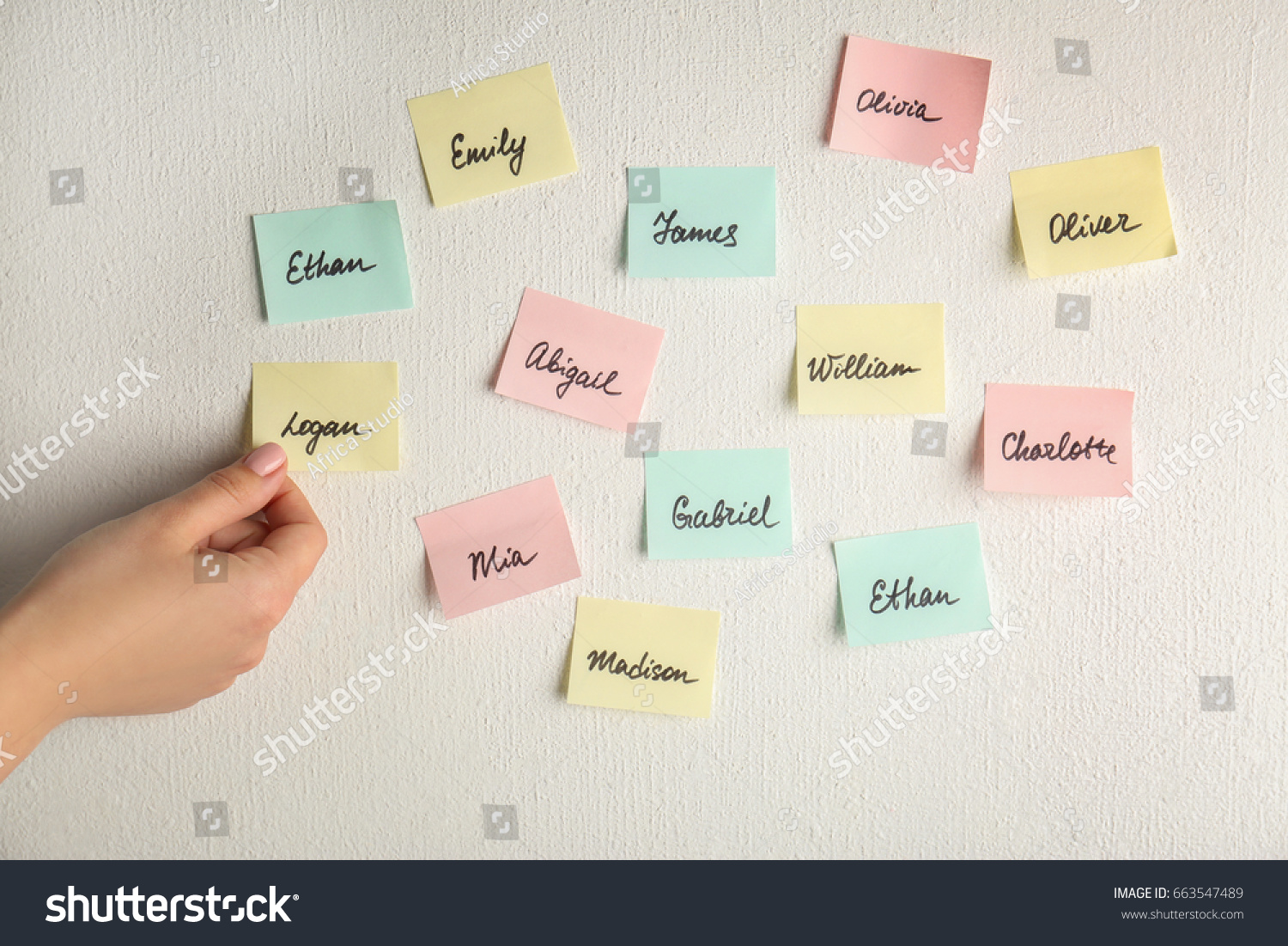 Female hand and paper stickers with different names on white wall. Concept of choosing baby name #663547489
