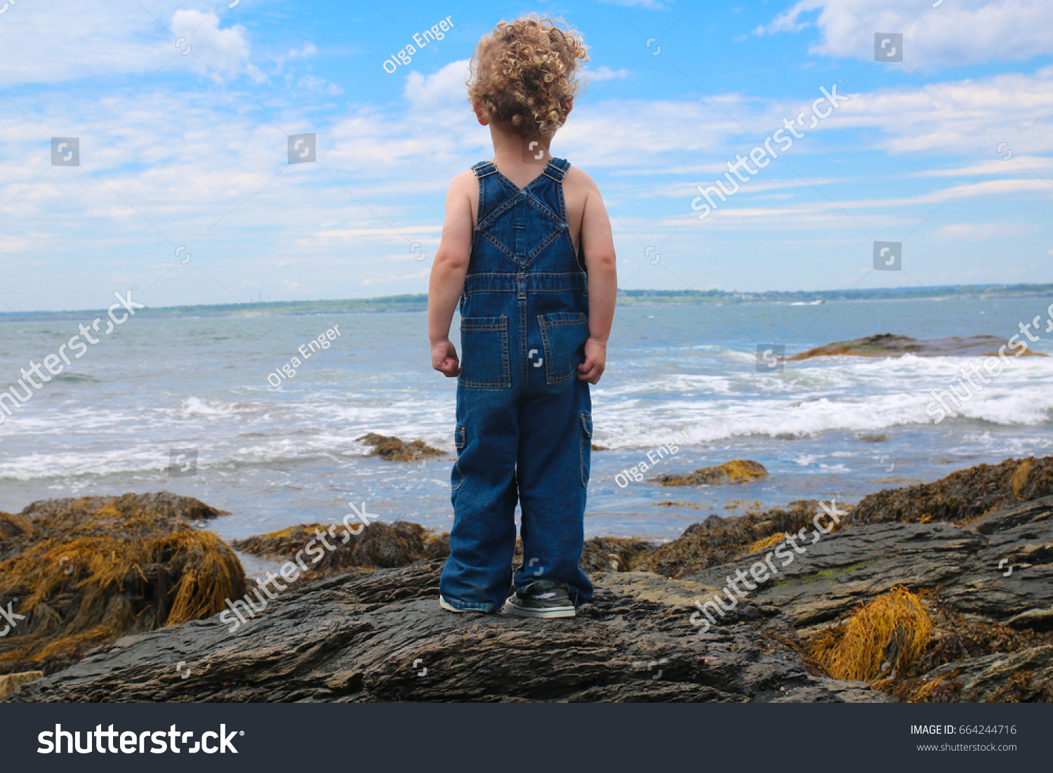 A little boy is looking out at the large ocean, standing on rocks. It's a big world and the child's future has endless possibilities. Courage, future, inspiration, goals, conquer your fear, aspiration #664244716