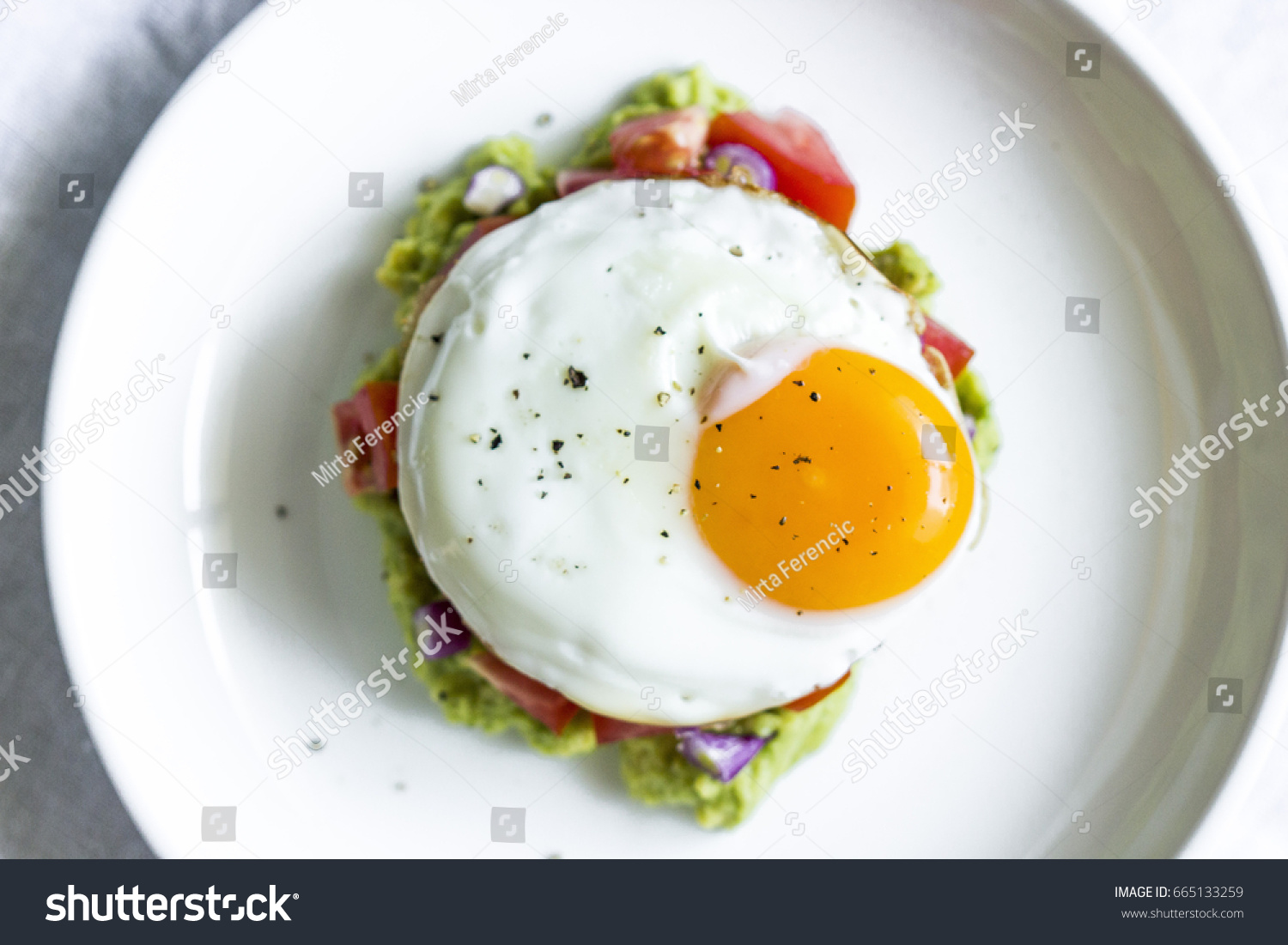 egg sunny side up on a bed of guacamole 
egg sunny side up on tomato tartar with avocado #665133259