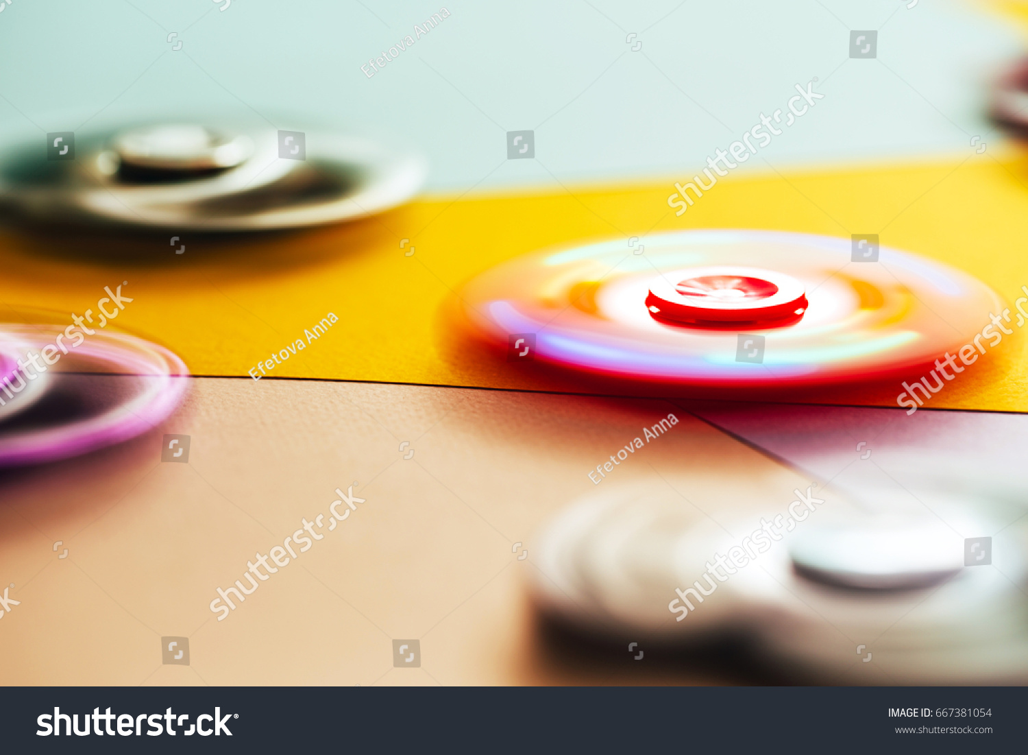 Silver fidget spinner rotating on multicolored background. #667381054