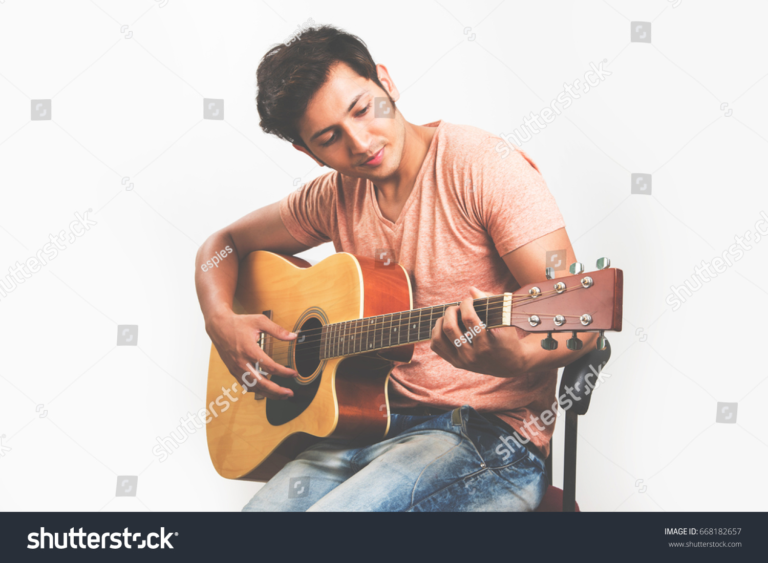 Indian/Asian young man playing Guitar, sitting against white background #668182657