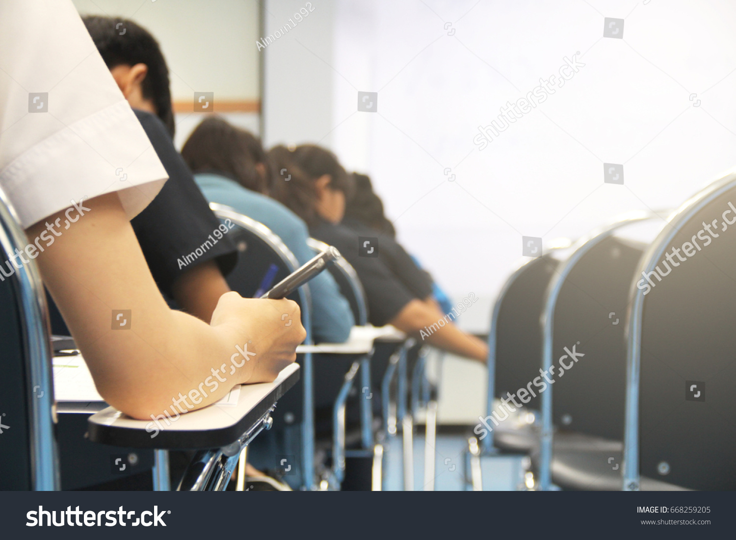 Hands university student holding pen writing /calculator doing examination / study or quiz, test from teacher or in large lecture room, students in uniform attending exam classroom educational school. #668259205