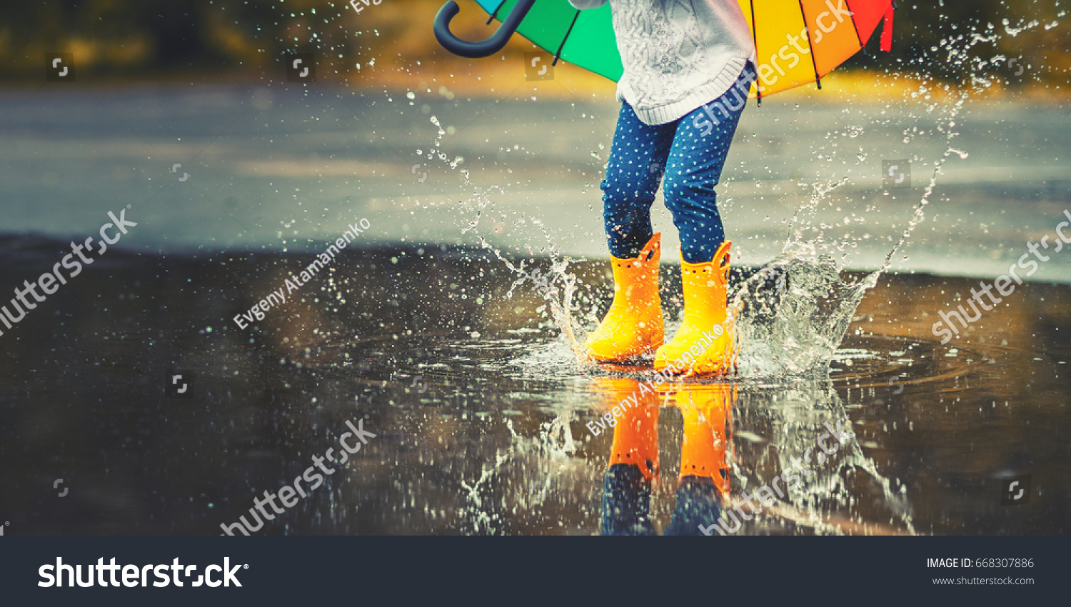 Feet of child in yellow rubber boots jumping over a puddle in the rain
 #668307886