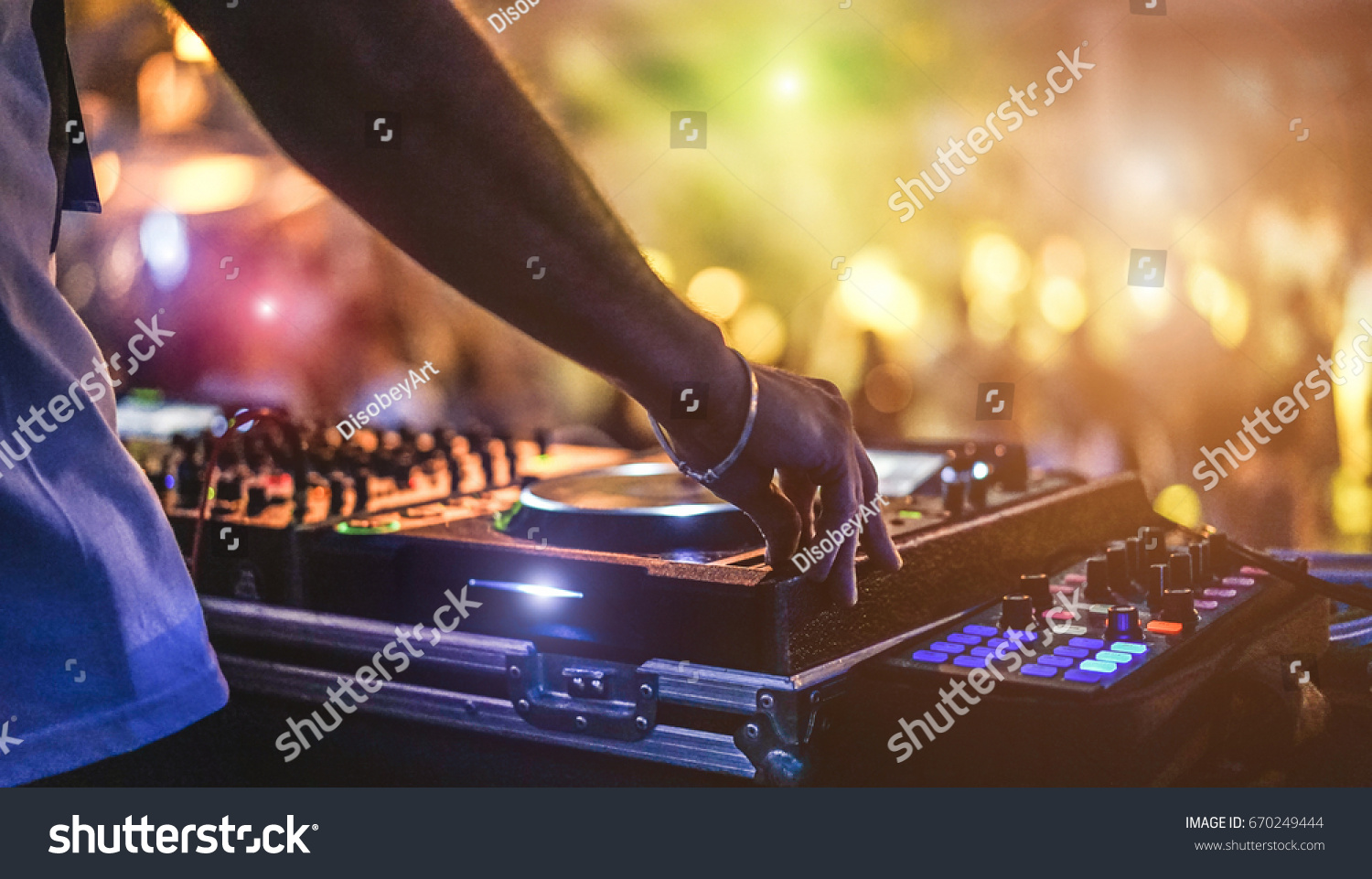 Dj mixing outdoor at beach party festival with crowd of people in background - Summer nightlife view of disco club outside - Soft focus on hand - Fun ,youth,entertainment and fest concept #670249444