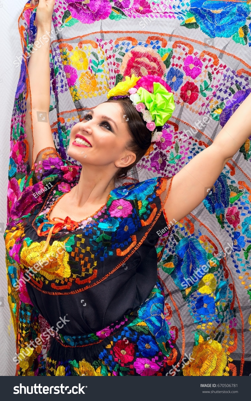 beautiful smiling mexican woman in traditional mexican dress hands up holding the skirt as a background like peacock #670506781