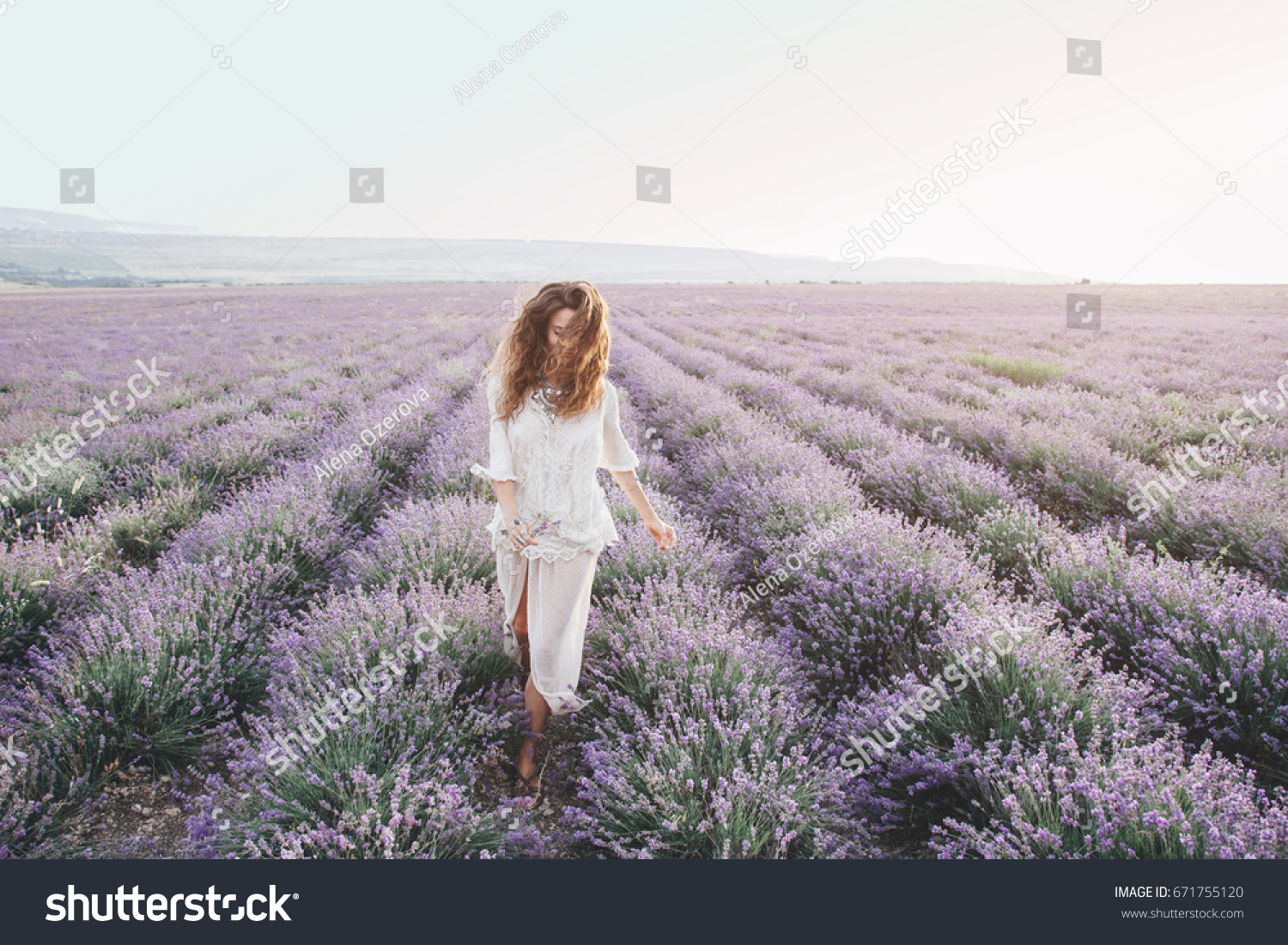 Beautiful model walking in spring or summer lavender field in sunrise backlit. Boho style clothing and jewelry. #671755120