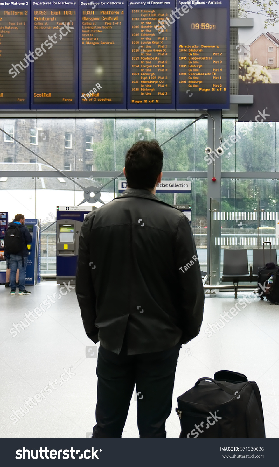 EDINBURGH, SCOTLAND - JUNE 20, 2017 : Haymarket Train Station interior showing departure board, unidentified traveller looking at departure board in foreground. #671920036