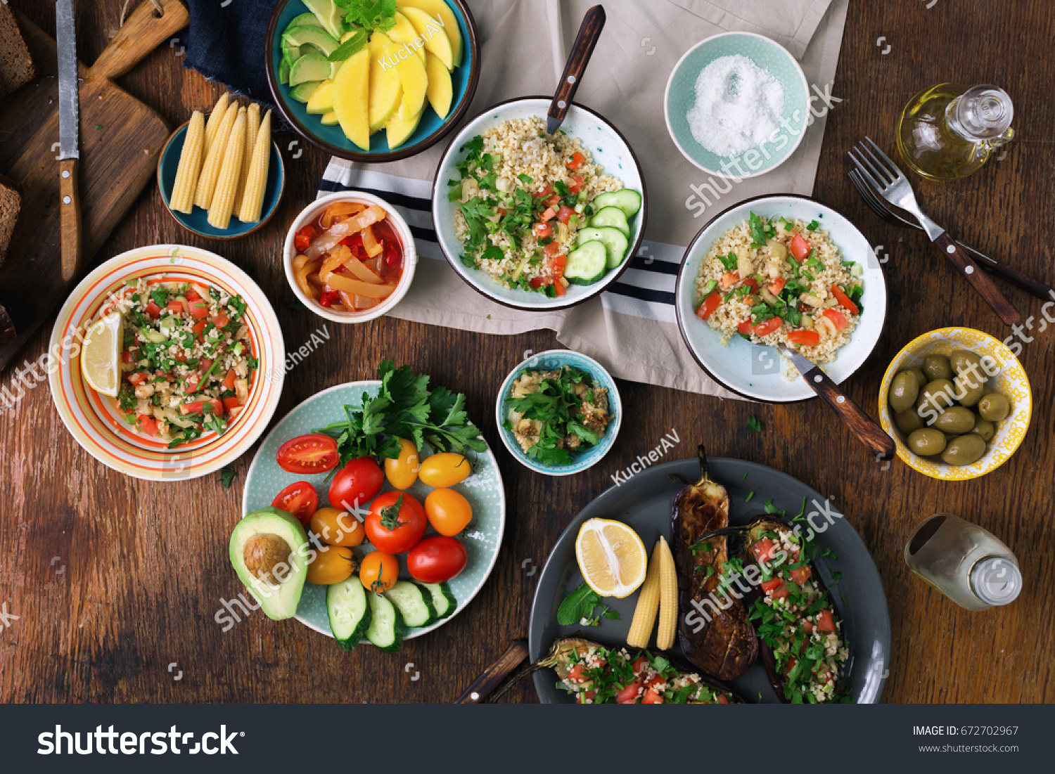 Vegetarian food concept. Set of healthy vegetarian food, salad with bulgur porridge and vegetables, stuffed eggplant, vegetables, mango, avocado and snacks on a wooden table, top view #672702967