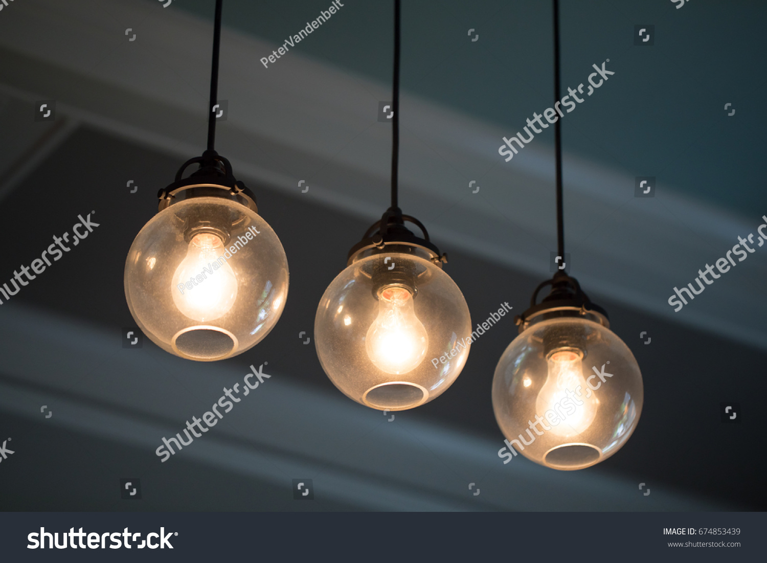 Close up midcentury modern remodeled home dining living room ceiling chandelier with three hanging incandescent illuminated light bulbs in glass globe orbs on black electrical cable with crown molding #674853439