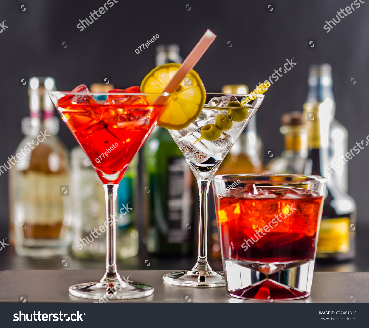 Colorful drink on the background of bottles in original shapes, cocktail drink with ice cubes, party night #677461306