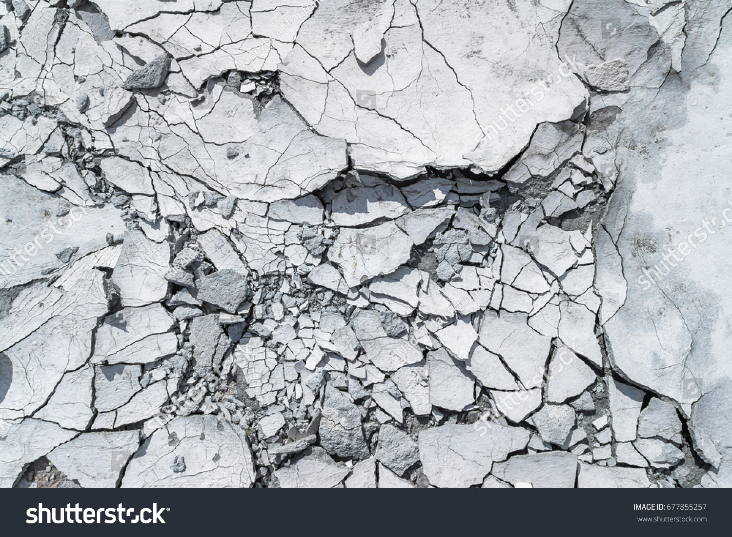Cracked concrete texture background. Grey surface with cracks close up. A lot of pieces of splintered plaster. Abstract concept of split, dissent, disagreement, discord. Sunny day with shadows. #677855257