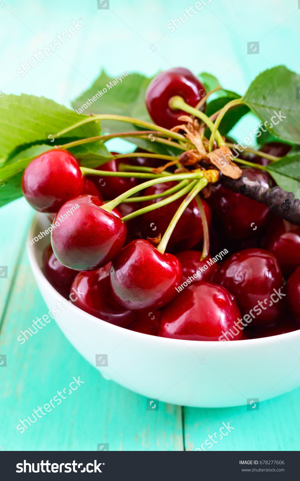 Ripe juicy red cherries in a ceramic bowl on a bright wooden background.  Vertical view #678277606