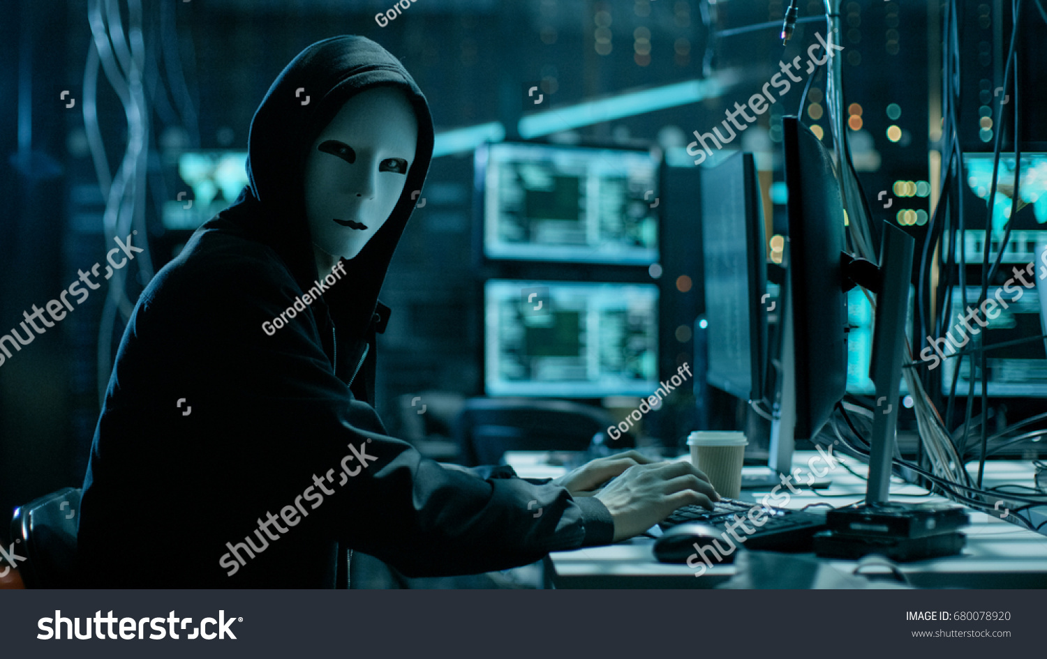 Masked Hacker is Using Computer for Organizing Massive Data Breach Attack on Corporate Servers. They're in Underground Secret Location Surrounded by Displays and Cables. #680078920