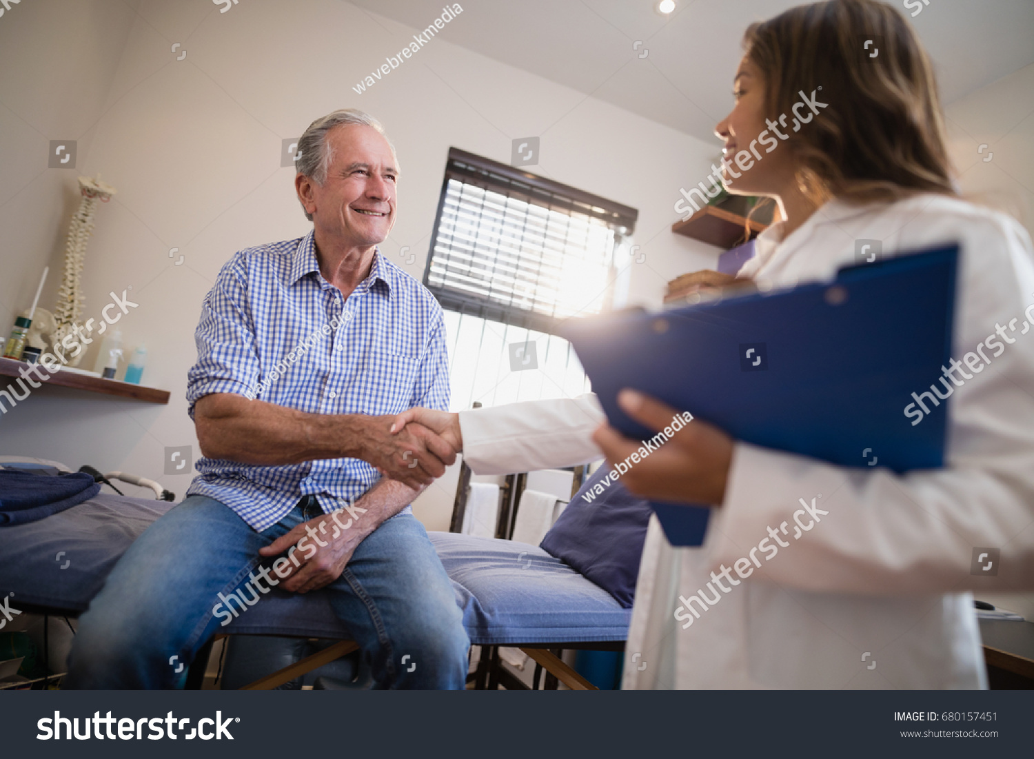 Low angle view of female therapist and senior male patient shaking hands at hospital ward #680157451