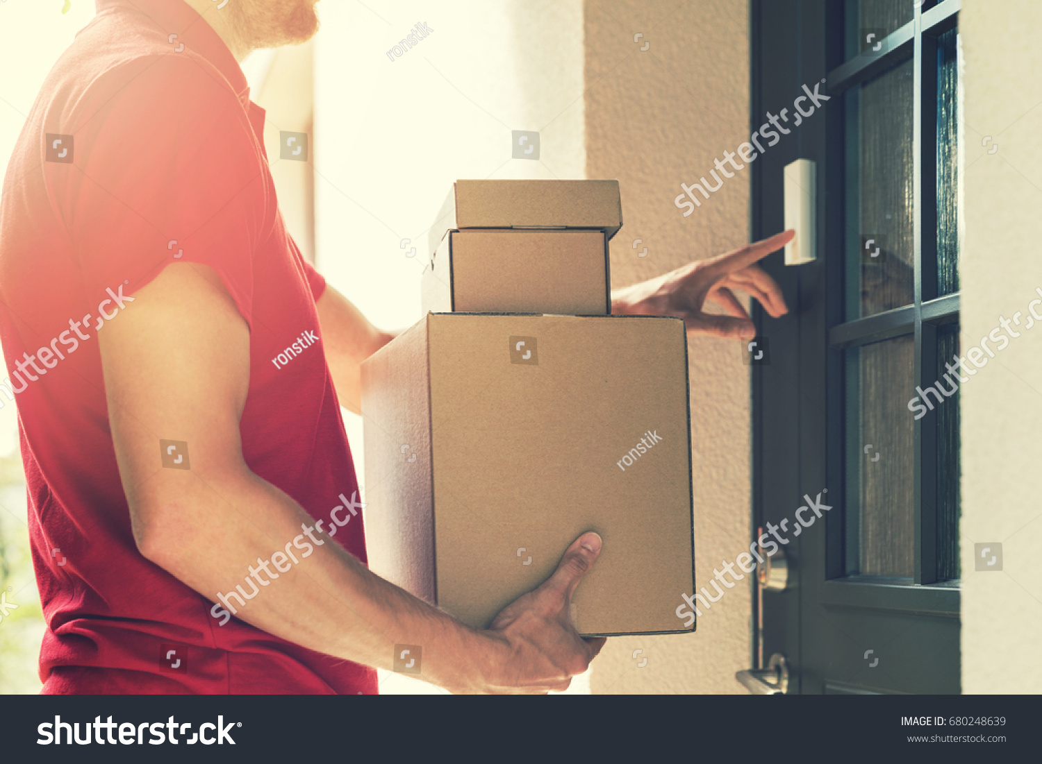 delivery service courier ringing the house doorbell with boxes in hands #680248639