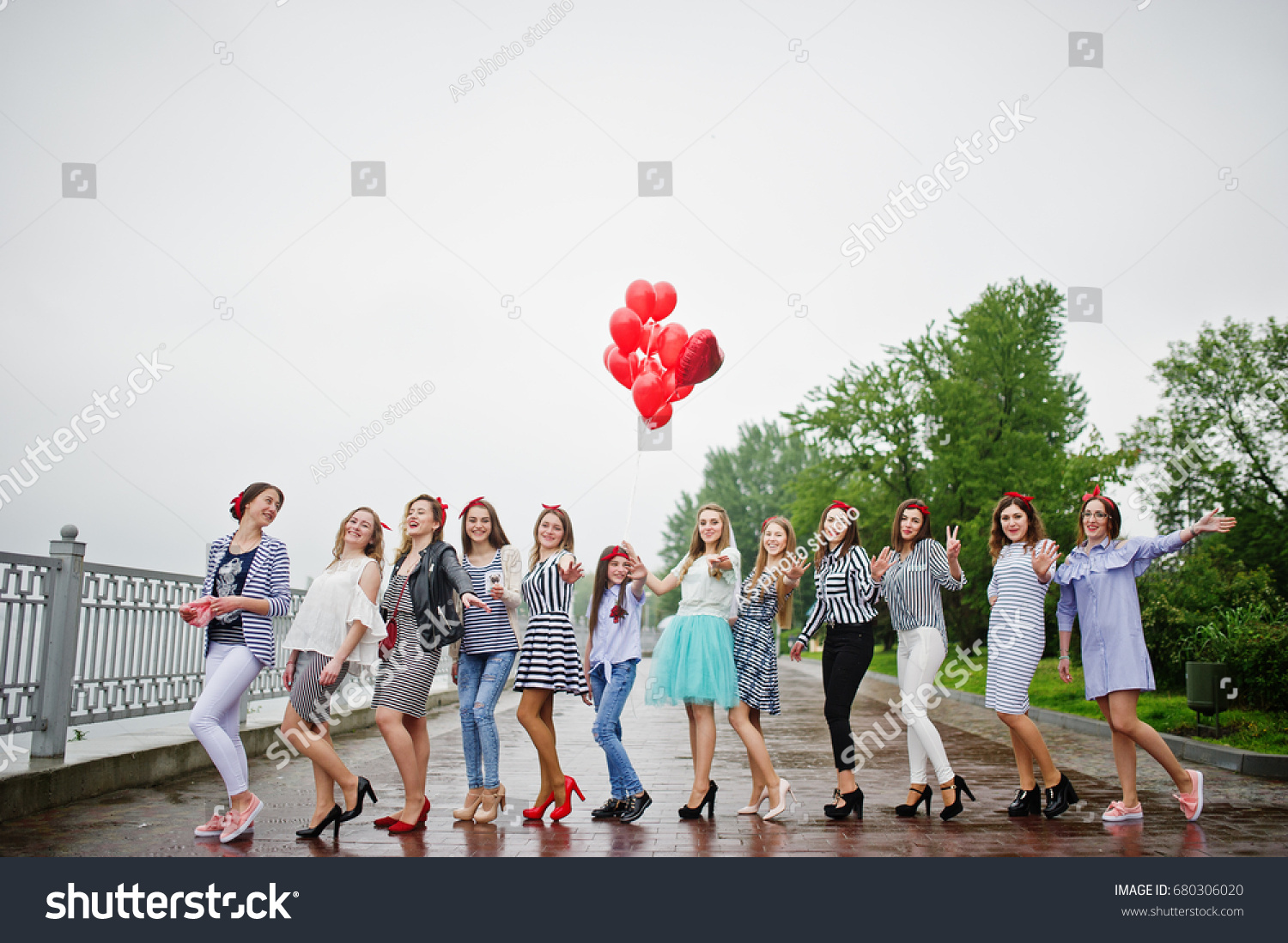 Eleven amazingly-looking braidsmaids with stunning bride posing with red heart-shaped balloons on the pavement against the lake in the background. #680306020