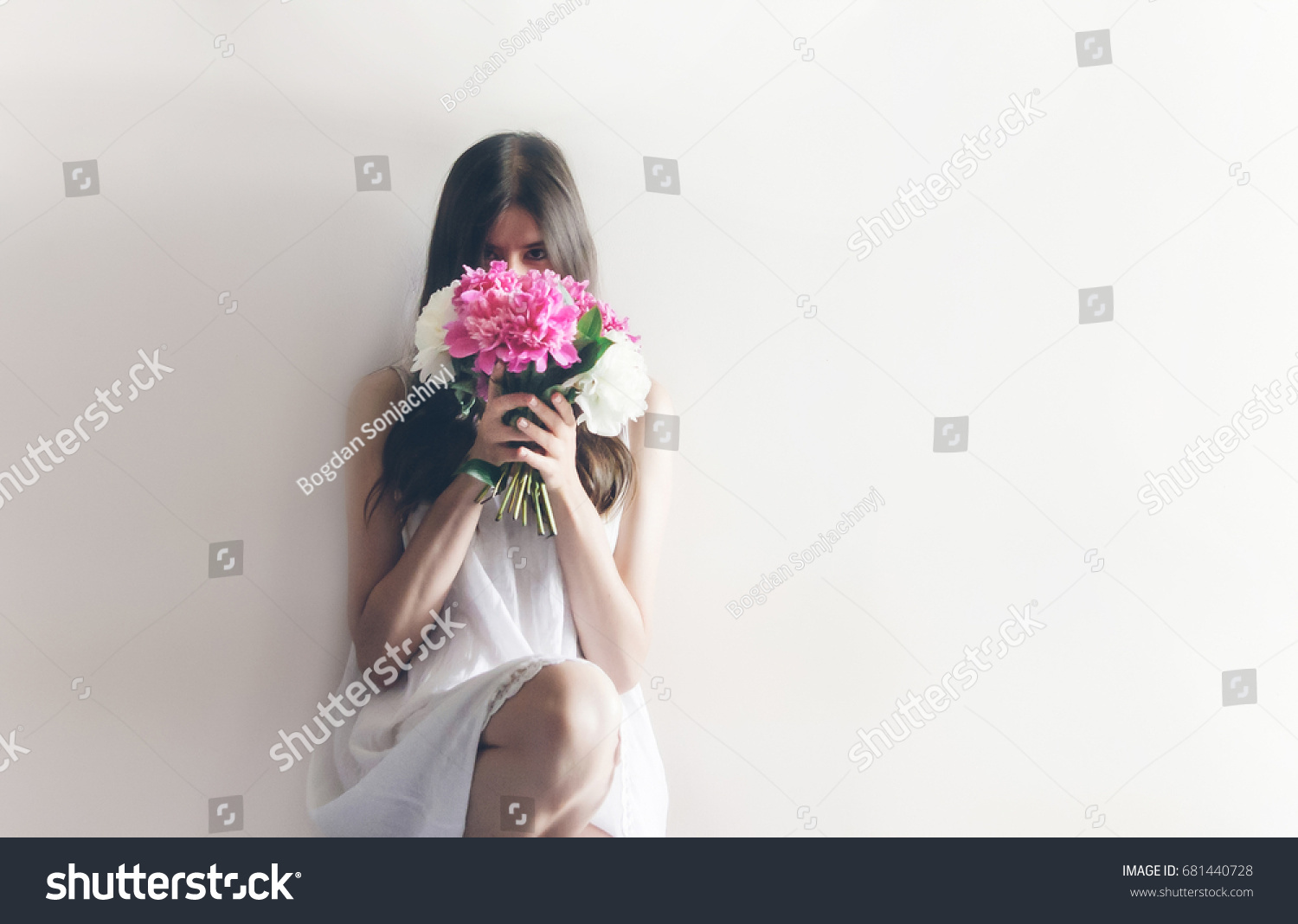 hipster woman in white dress holding pink bouquet of peonies in white room. boho bride with peony bouquet in front, relaxing in morning, space for text. spring girl with flowers #681440728