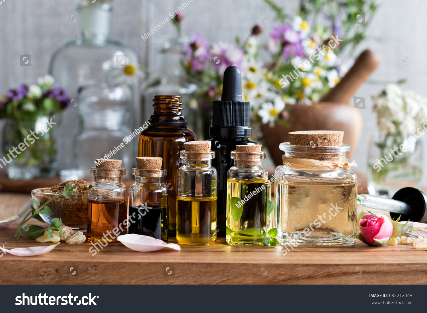 Selection of essential oils, with herbs and flowers in the background #682212448