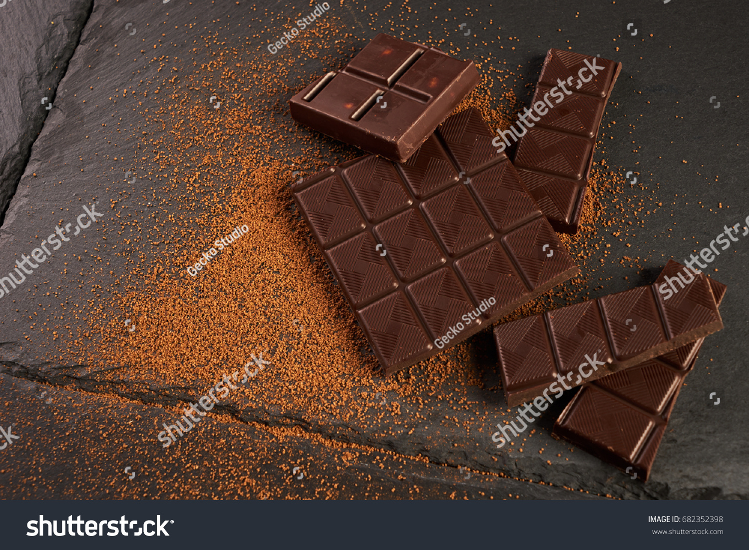 Close-up of broken chocolate pieces and cocoa powder on dark stone background with copy space. #682352398