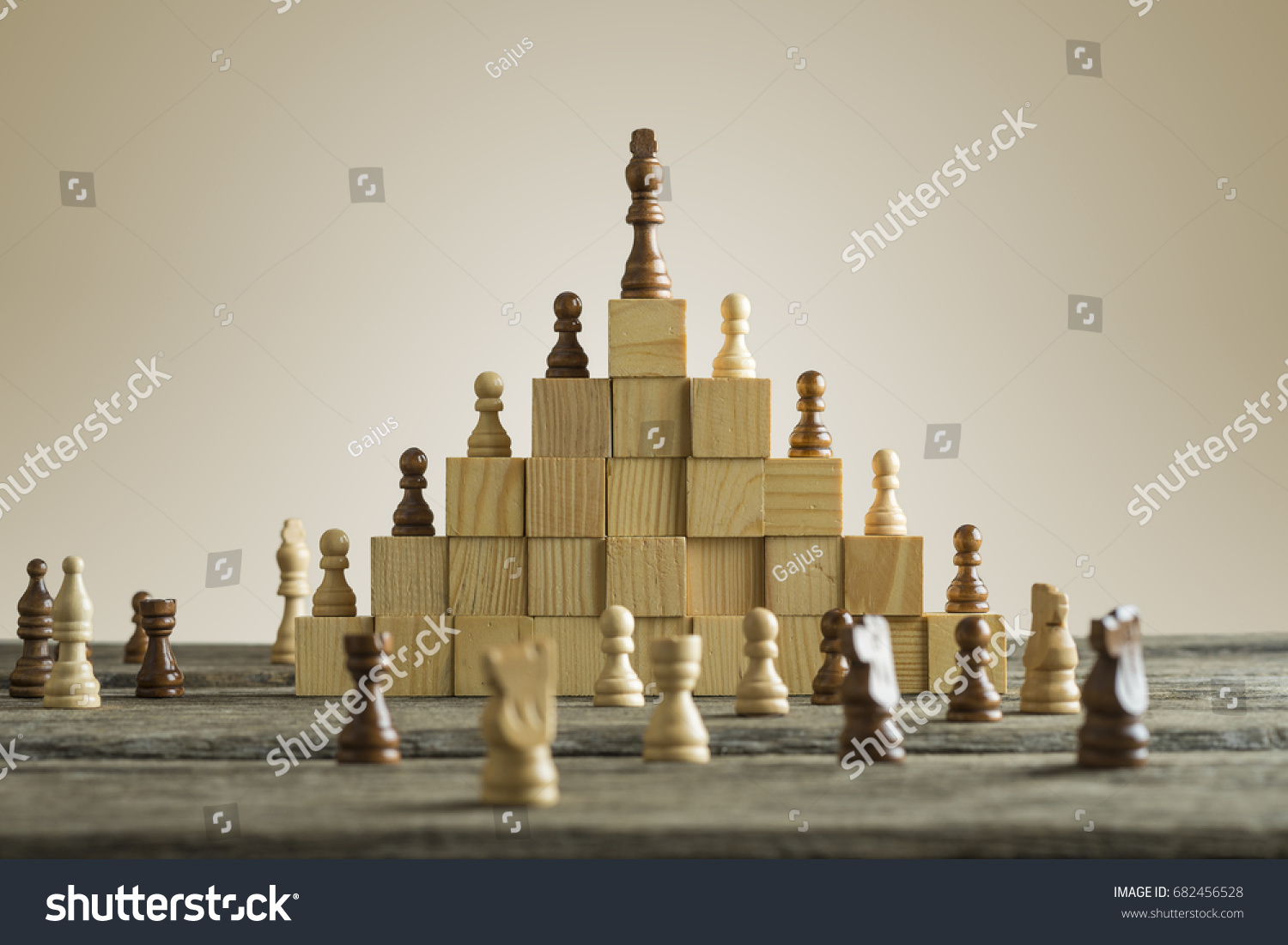 Business hierarchy; ranking and strategy concept with chess pieces standing on a pyramid of wooden building blocks with the king at the top with copy space. #682456528