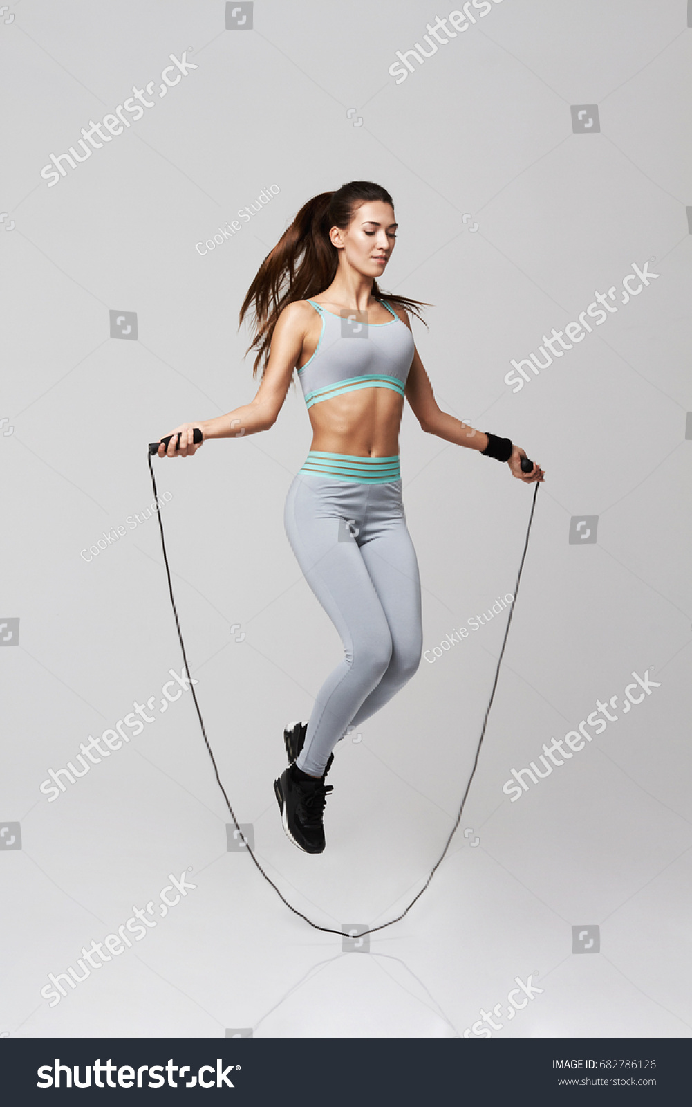 Young sportive beautiful girl doing exercises with jumping rope over white background. #682786126
