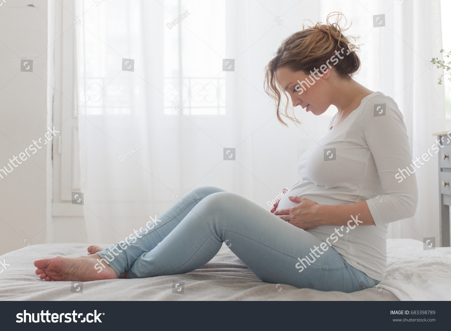 Pregnant woman sitting on bed looks at the belly #683398789