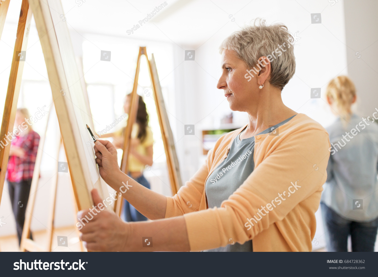 art school, creativity and people concept - happy senior woman artist with easel and pencil drawing picture at studio #684728362